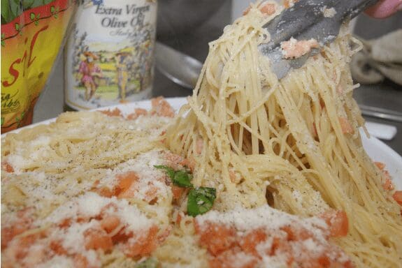 Tongs lifting spaghetti with tomato and Parmesan
