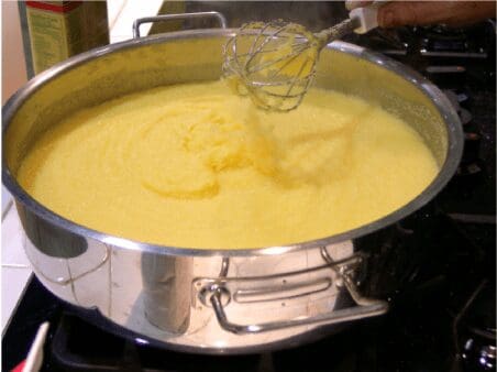 Whisk stirring creamy polenta in stainless pot
